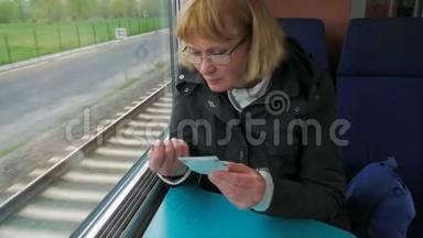 一个女人坐在窗边的高速列车上检查车票。